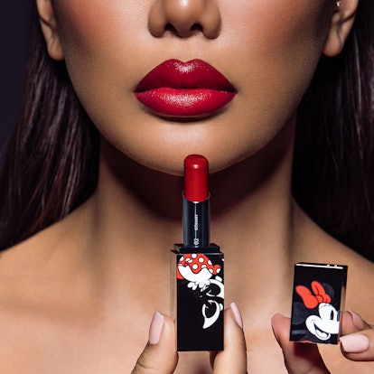 A woman holds up a red lipstick with Minnie Mouse on it from the House of Sillage Disney makeup coll...