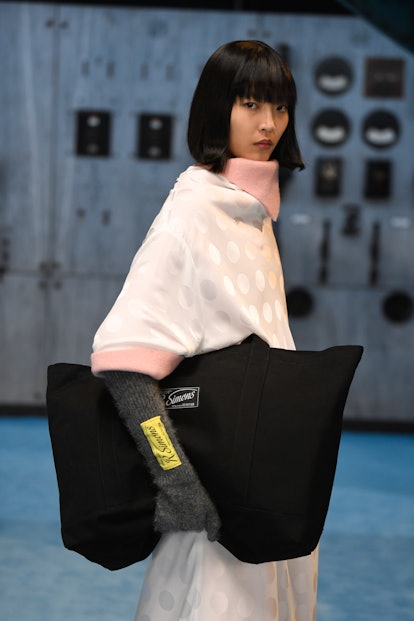 A model wearing a white sweater dress and black bag at Raf Simons fall 2021 runway show