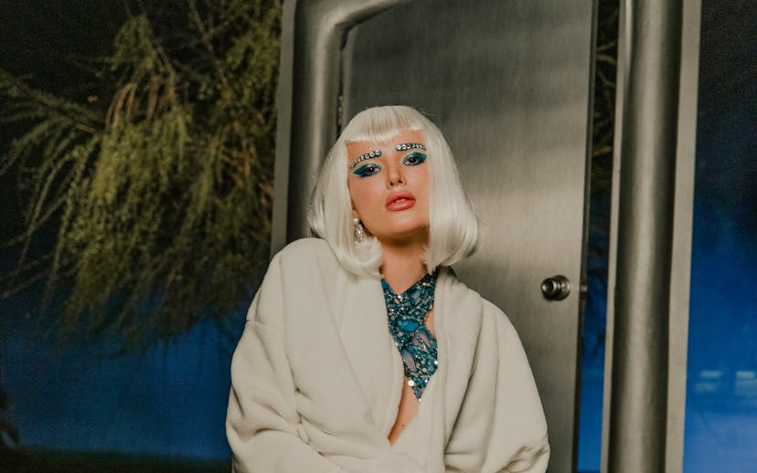 A portrait of Bella Thorne. The singer wears a platinum bob wig, and a sparkly teal evening gown wit...