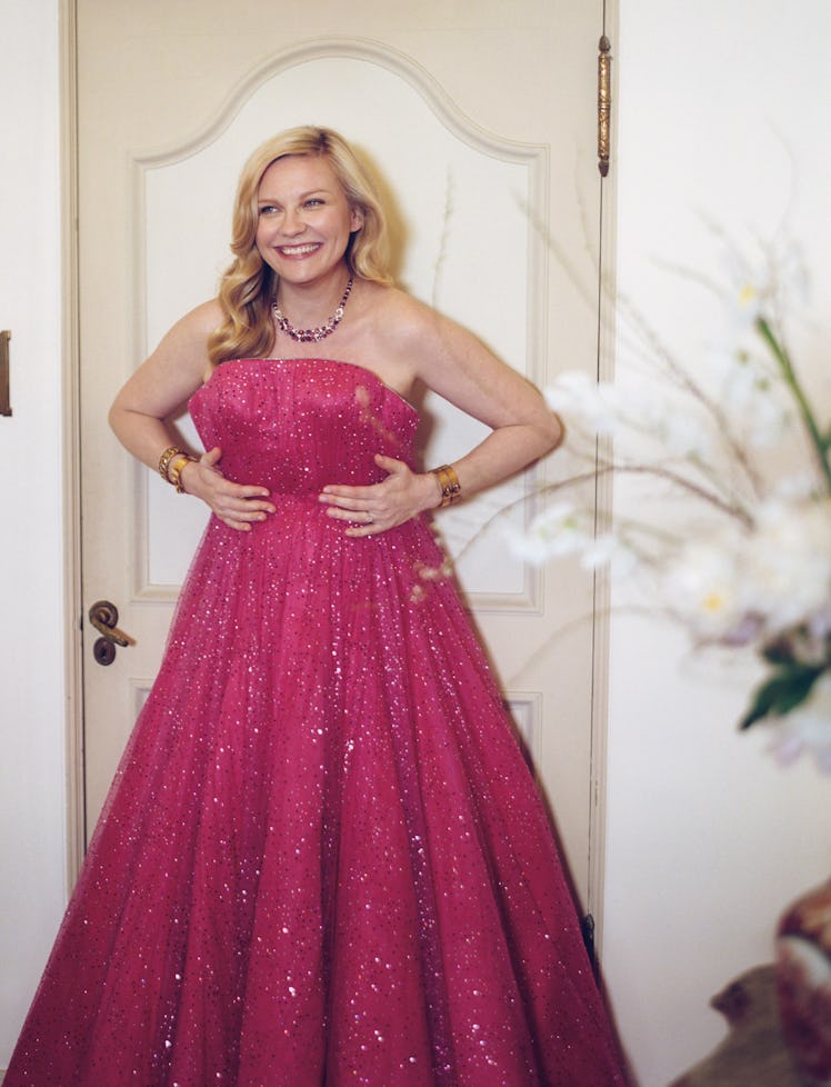Kirsten Dunst posing leaned against doors while smiling in a pink glitter maxi princess dress