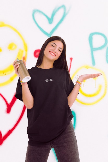 Charli D'Amelio with a spray can in her hand in front of a graffitied wall for Pura Vida.
