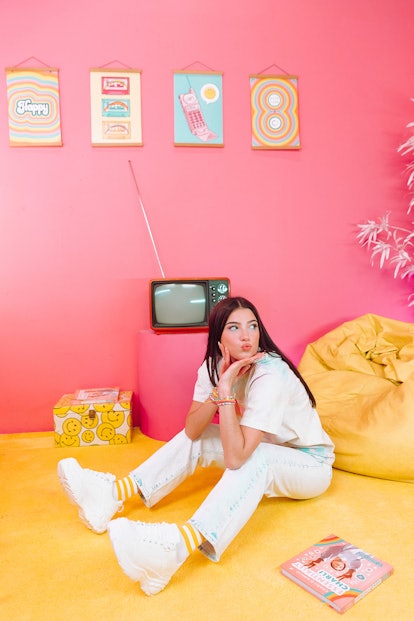 Charli D'Amelio  sitting on the floor of a pink and yellow room for Pura Vida.