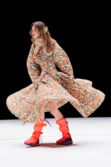 Model dancing in a Kenzo show in a long floral dress and orange boots 