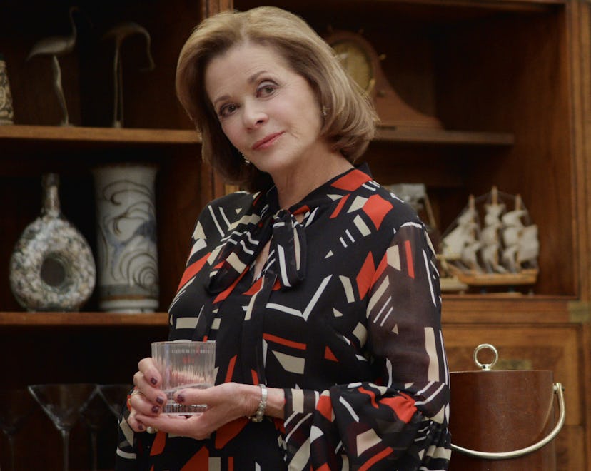 Jessica Walter as Lucille Bluth is wearing a black, red and white dress and holding a rocks glass.