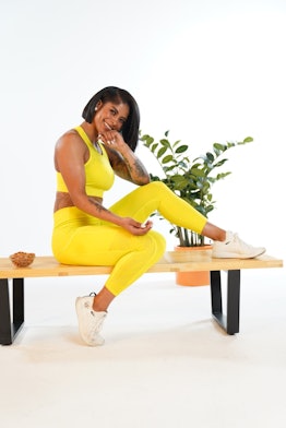 Massy Arias wearing yellow fitness clothes and posing on a bench
