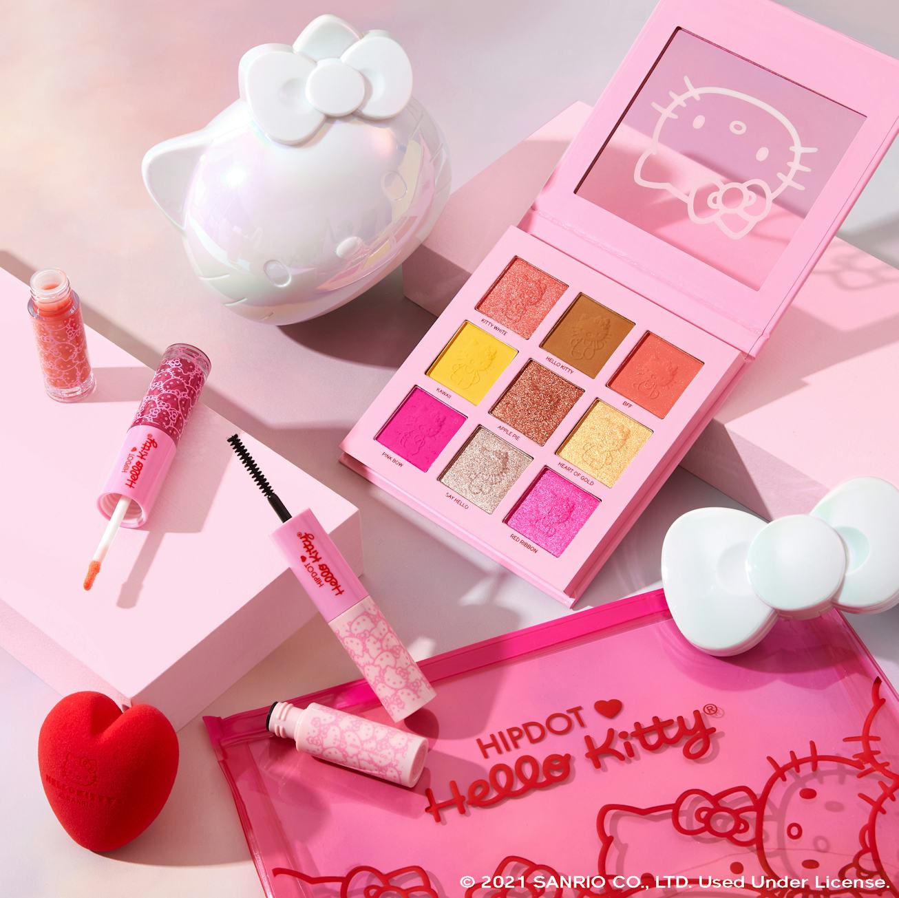 HipDot Hello Kitty products, including an eyeshadow palette and mascara, are laid out on a white bac...