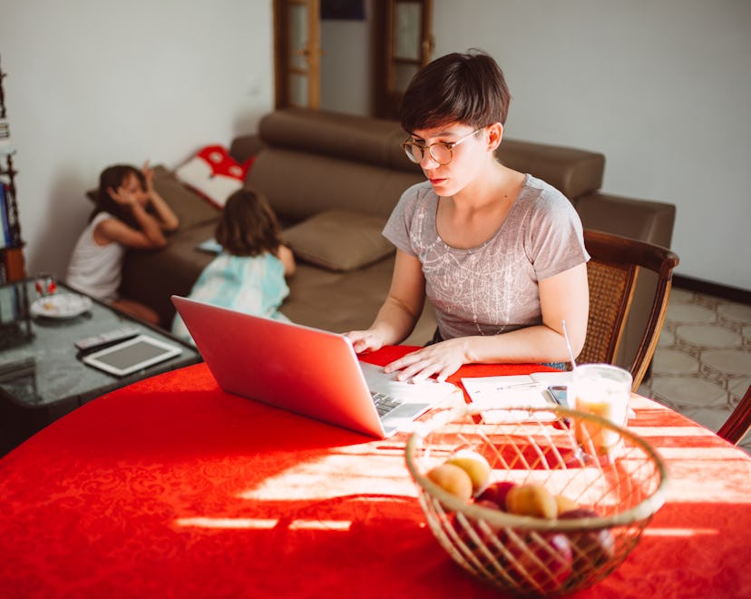 Mother on a laptop doing her taxes while her two children play in the background