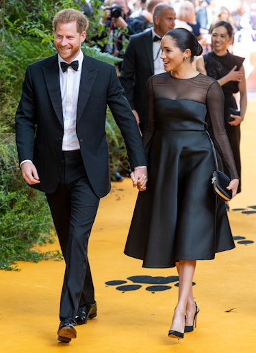 Meghan Markle in a black dress and Prince Harry in a black suit and white shirt walking and smiling