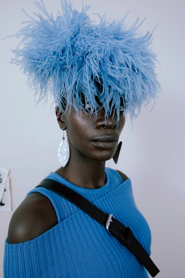 A model in a blue sweater with both shoulders exposed and a blue feathered head accessory by Thebe M...