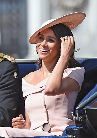 Meghan Markle in a beige dress and hat smiling and sitting in a carriage