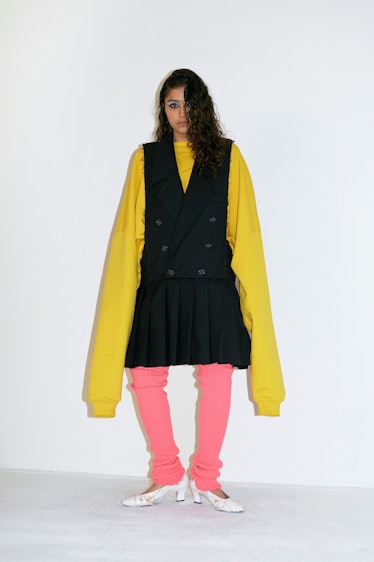 A model in a black vest dress, yellow oversized sweater and pink pants by Vaquera