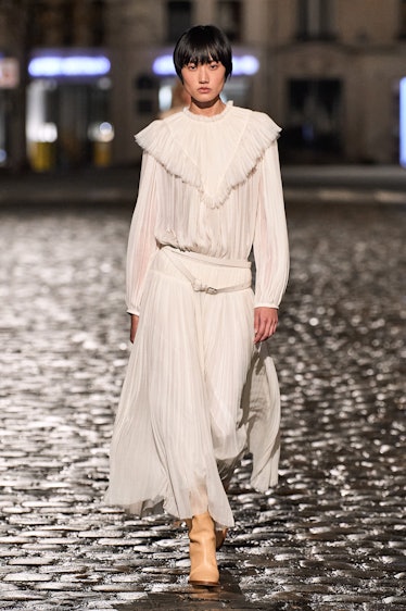 A model walking the runway in a white pleated blouse and skirt by Chloé