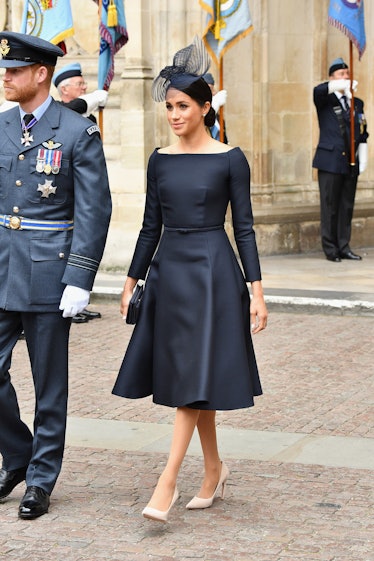 Meghan Markle in a black dress and hat, and beige heels and Prince Harry in a uniform