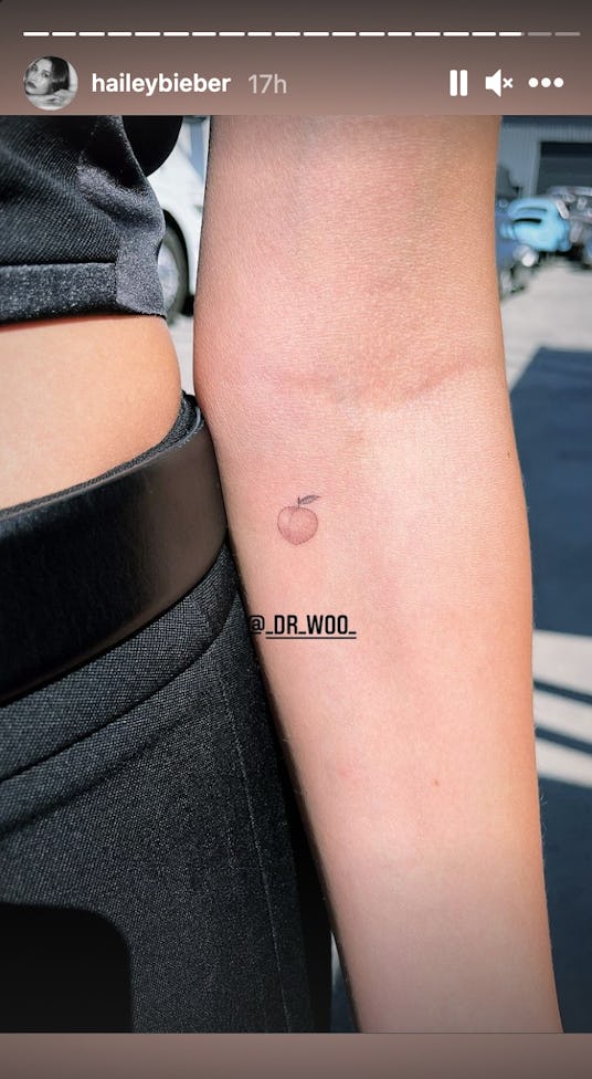 Hailey Bieber holds out her forearm, showing the peach tattoo added to her skin by Dr. Woo.
