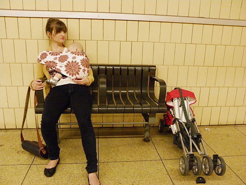 A woman sitting on a bench and holding her baby with the help of a carrier on her chest