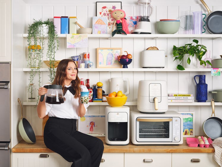 Drew Barrymore sits on a kitchen counter with some Beautiful Kitchenware around her.