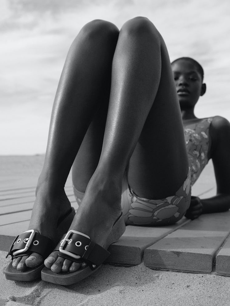 A model lying on the beach while wearing '90s-inspired minimalist sandals.