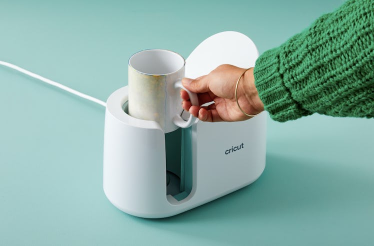 A woman puts a mug into the Cricut Mug Press to make a DIY mug. 