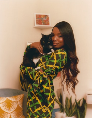Sydnee Washington holding her cat in a black dress with green and yellow patterns of women's silhoue...