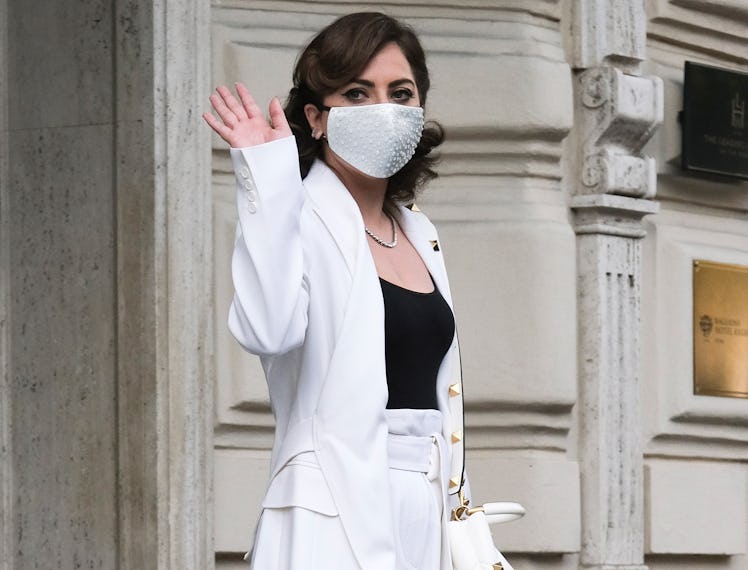 Lady Gaga in a black top and a white suit, with a white face mask waving