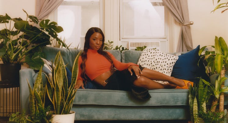 Sydnee Washington posing on a green couch, wearing an orange crop top and black skirt 