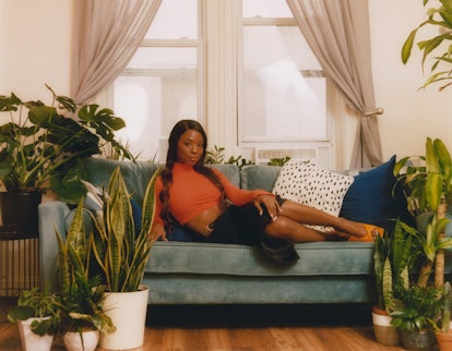 Sydnee Washington posing on a green couch, wearing an orange crop top and black skirt 
