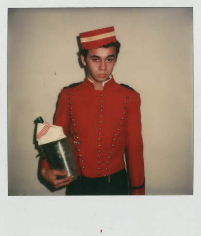 Young Christian Louboutin in a red hotel page uniform with a champagne holder