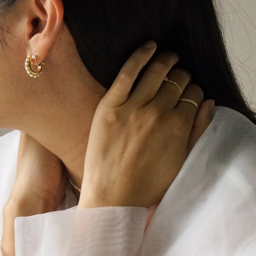 Close up of woman wearing pearl hoop earrings and gold rings on her hand