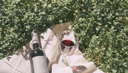 A wine glass and bottle on a white picnic blanket