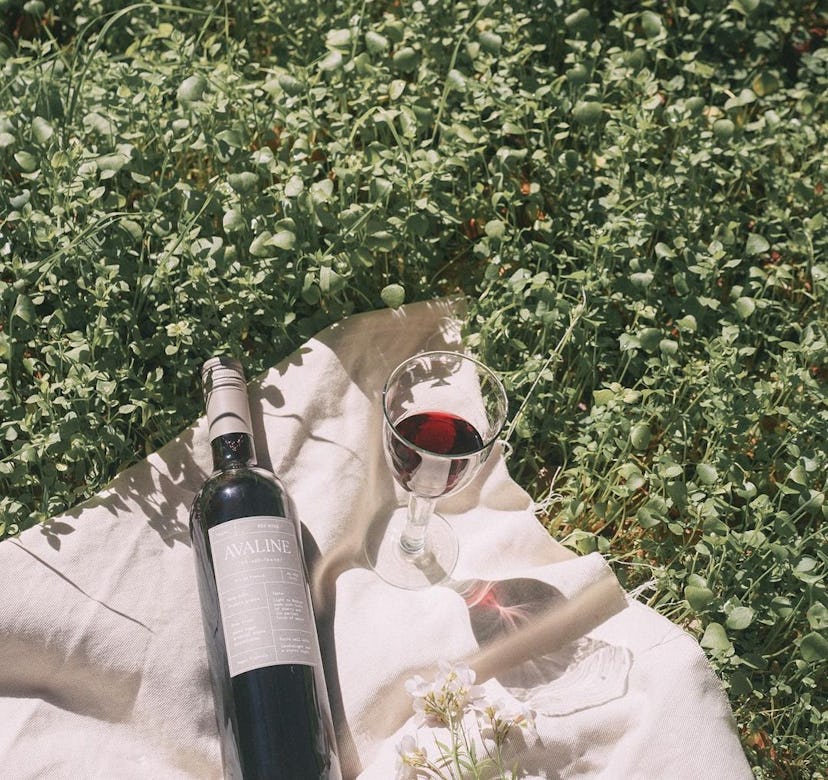 A wine glass and bottle on a white picnic blanket