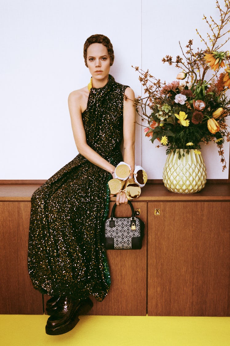 A model sitting on a cupboard in a black dress with multicolored spots on it by Loewe