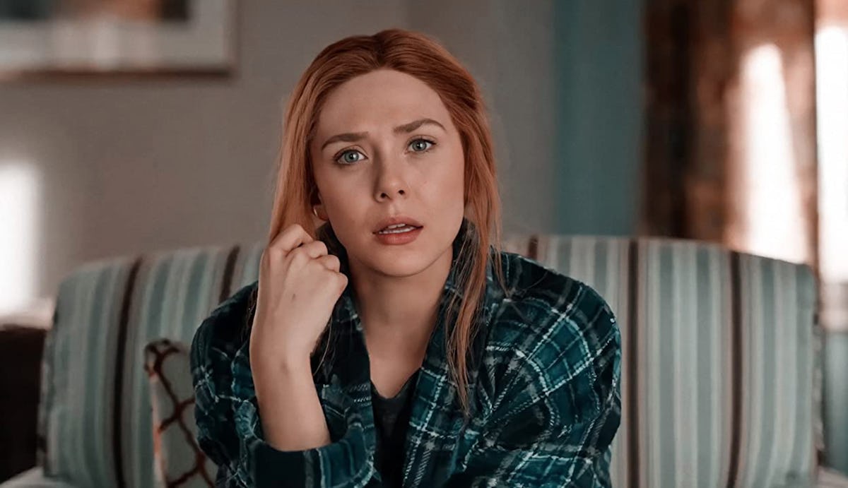 Elizabeth Olsen sits on a couch and looks shocked during an episode of 'WandaVision,' and sports a n...
