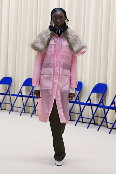 A model in a pink rain coat, black pants and a fur throw over the rain coat all by Nina Ricci