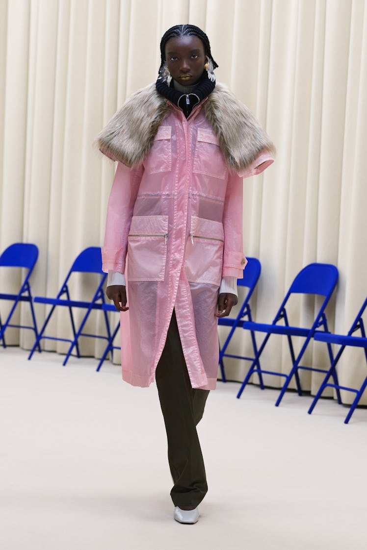 A model in a pink rain coat, black pants and a fur throw over the rain coat all by Nina Ricci