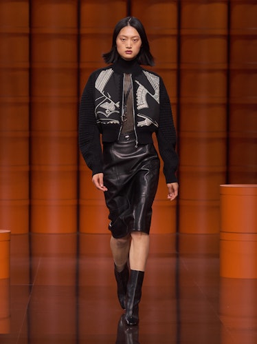A model in a black jacket, sheer top and black leather skirt by Hermès