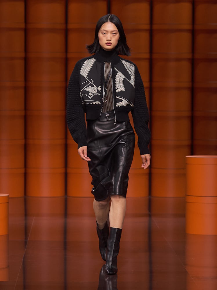 A model in a black jacket, sheer top and black leather skirt by Hermès