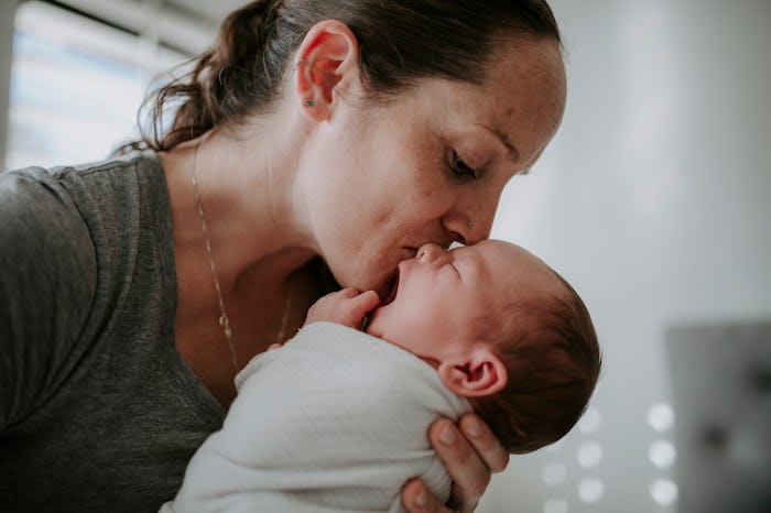mother kissing swaddled newborn