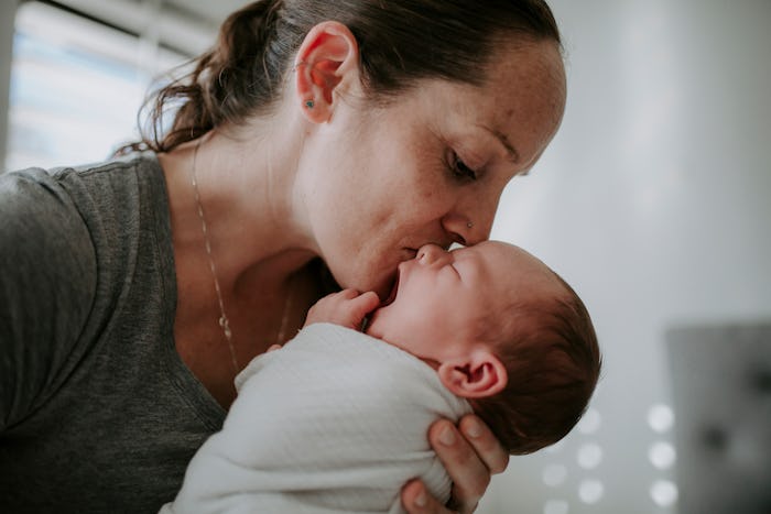 mother kissing swaddled newborn