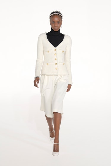 A model in a white blazer and skirt with a black turtleneck by Giambattista Valli