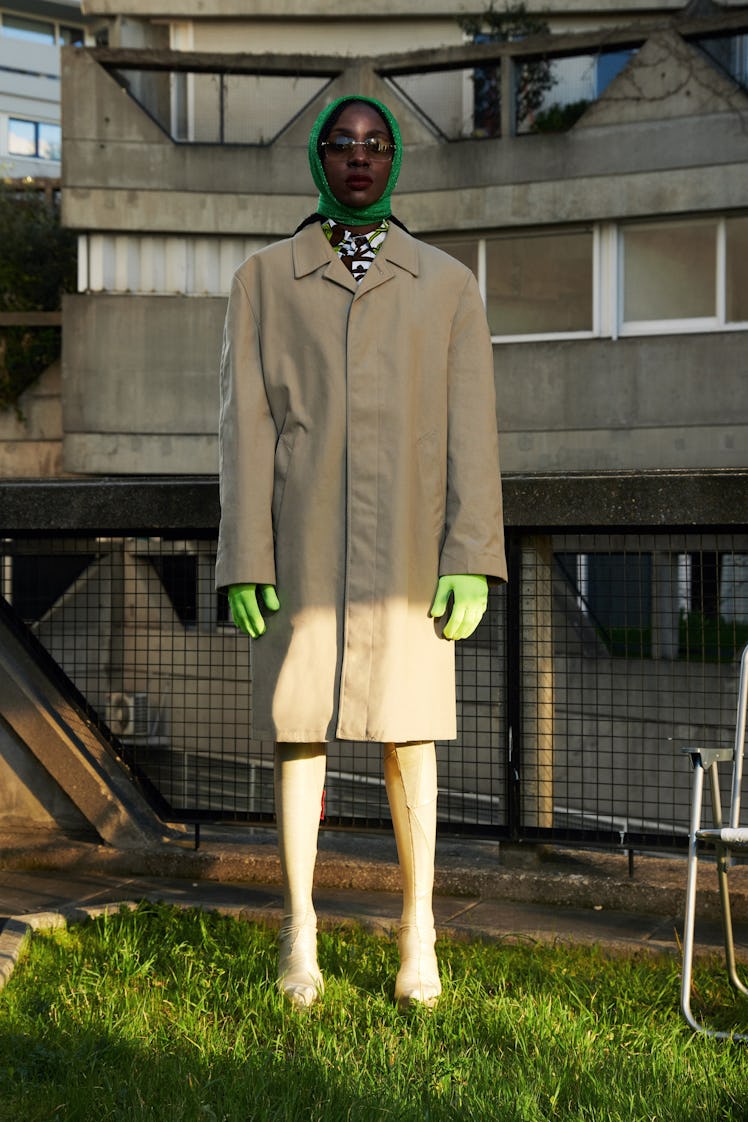A model in a beige trench coat, lime green gloves, a green headscarf and sunglasses by Xuly.Bët