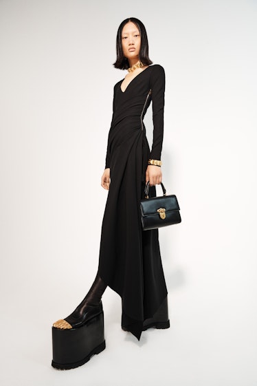 A model in a long black gown, embellished black platforms and a black bag by Schiaparelli