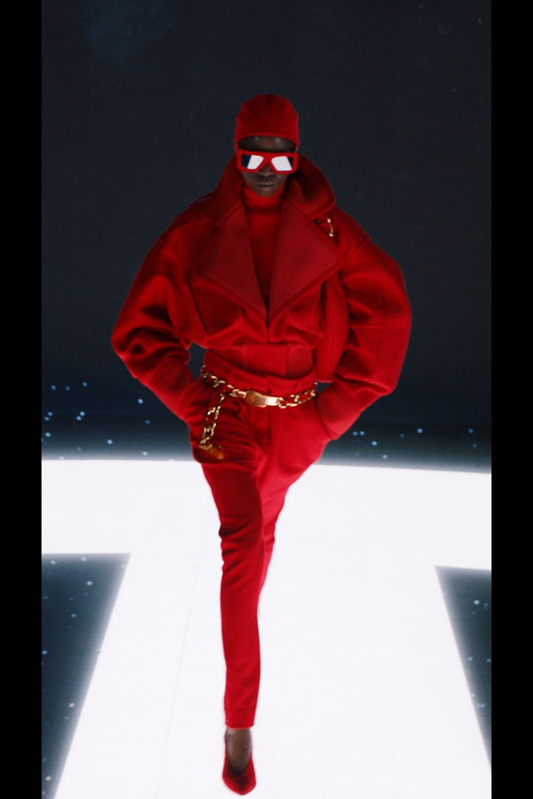 A model in a red jacket, pants, ski mask and sunglasses by Balmain 
