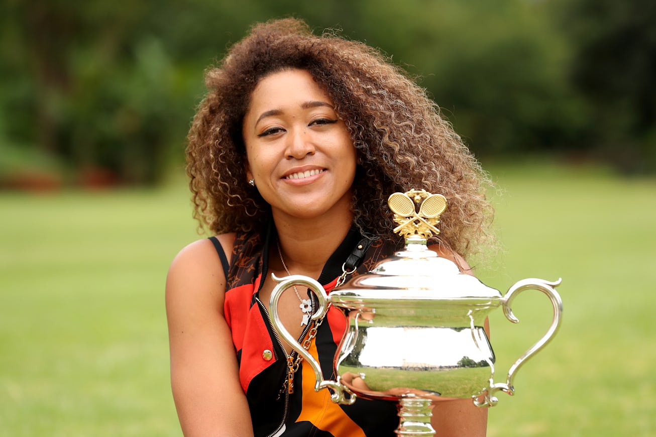 Naomi Osaka seated on grass with trophy