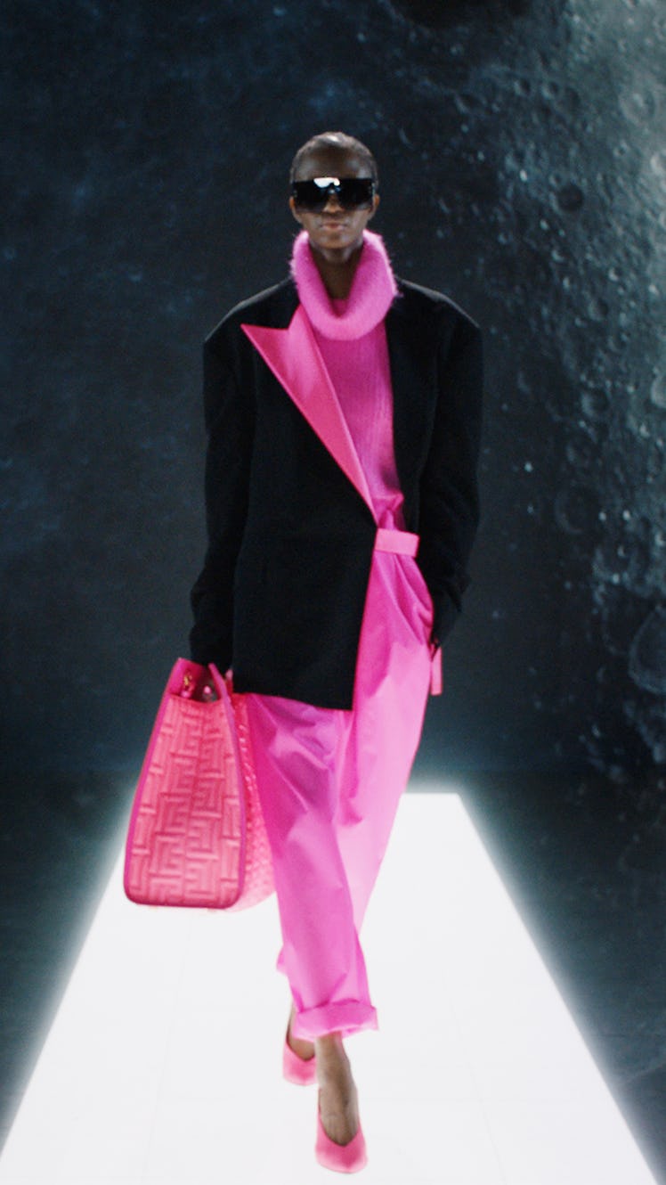 A model in a pink turtleneck, pink pants and bag, with a black coat by Balmain 