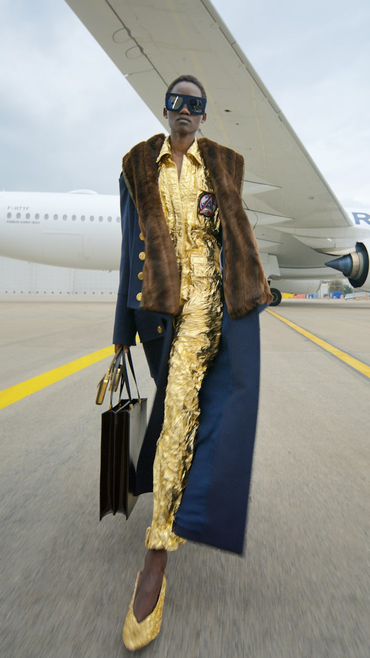 A model in a gold shimmery jumpsuit, sunglasses and a navy blue coat with fur by Balmain 