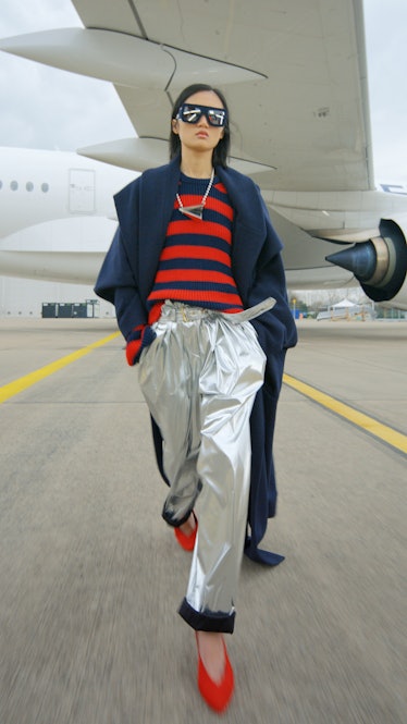 A model in a blue and red striped shirt, silver pants, sunglasses and blue coat by Balmain 