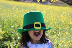 young girl in a field of flowers, wearing a leprechaun hat over her eyes