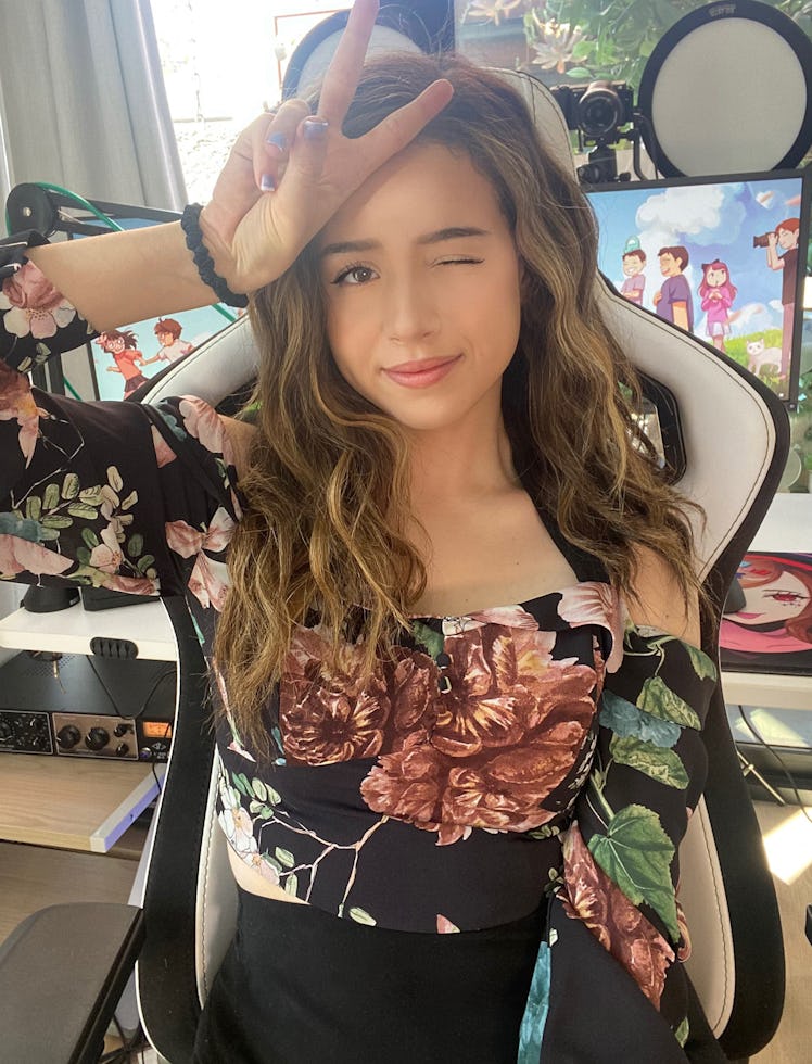 Imane “Pokimane” Anys sitting in a gaming chair, wearing a floral top and showing the "peace" sign 