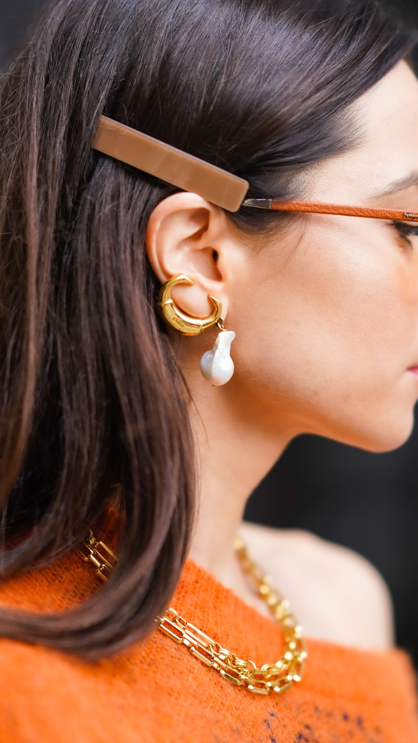 Julia Comil wears orange clear sunglasses, pearl earrings, a golden necklace, a one shoulder oversiz...
