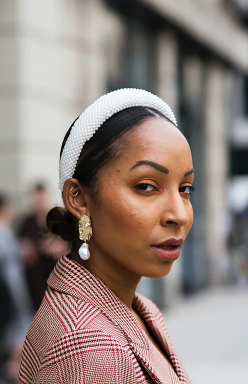 Guest wearing red and white checked blazer and oversized pearl Alice band headband is seen during Ne...
